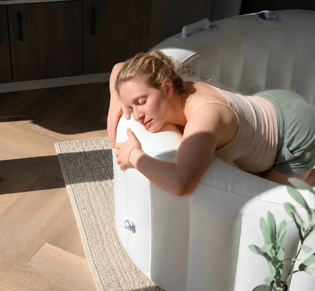 Zwangere vrouw leunt rustend op de zachte rand van een opblaasbaar bevalbad tijdens een waterbevalling thuis.